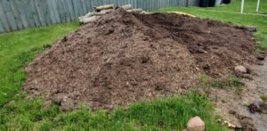 Photo shows a pile of mushroom soil that has been delivered outside the fence. Soil is one of the materials for garden beds that can be cheaply sourced from local companies. 